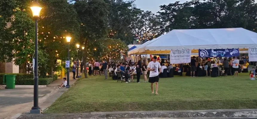 A pop-up at dusk: a large white tent of food stalls under string lights, families seated at tables on the grass, and a crowd moving between the stalls.