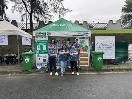 The green Trash to Cashback exchange tent with its crew standing outside it, My Basurero collection bins either side and a weighing scale on the ground.