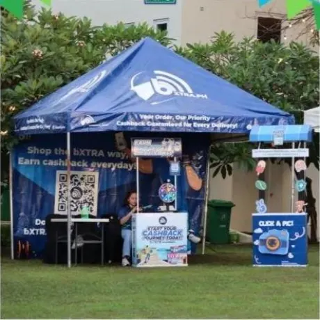 A bXTRA tent at the pop-up with a large bXCODE QR displayed on the counter panel and a staff member seated behind it.