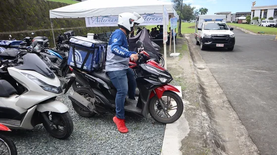 A bXTRA rider mounting his motorbike with a bXTRA Community Rider delivery box fitted, leaving the pop-up to make a delivery.